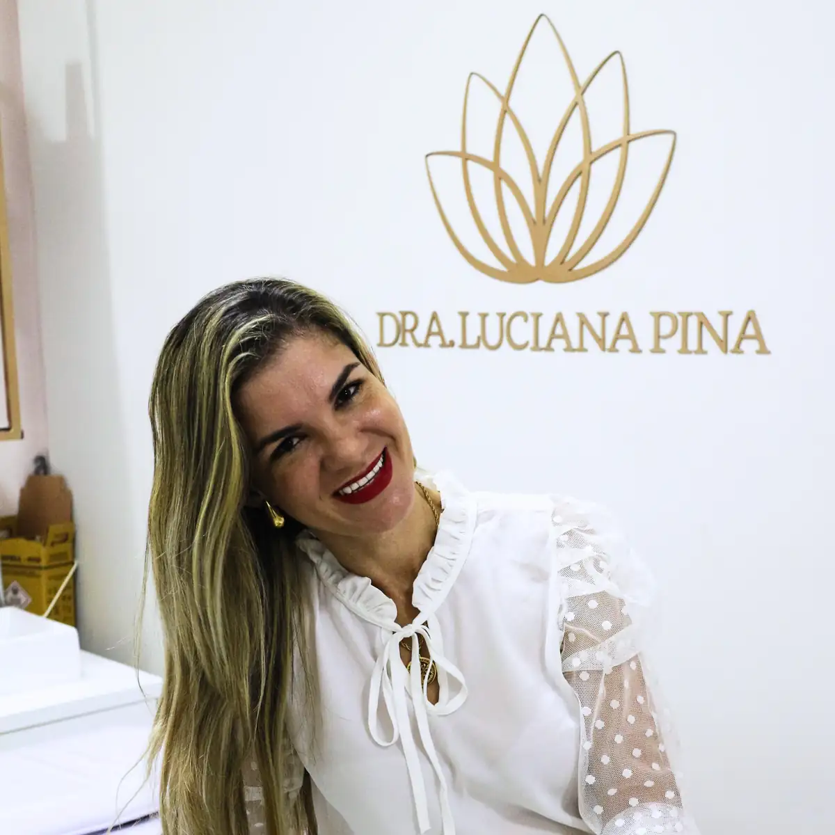 Dra. Luciana Pina sorrindo na clínica, com o logotipo da marca na parede